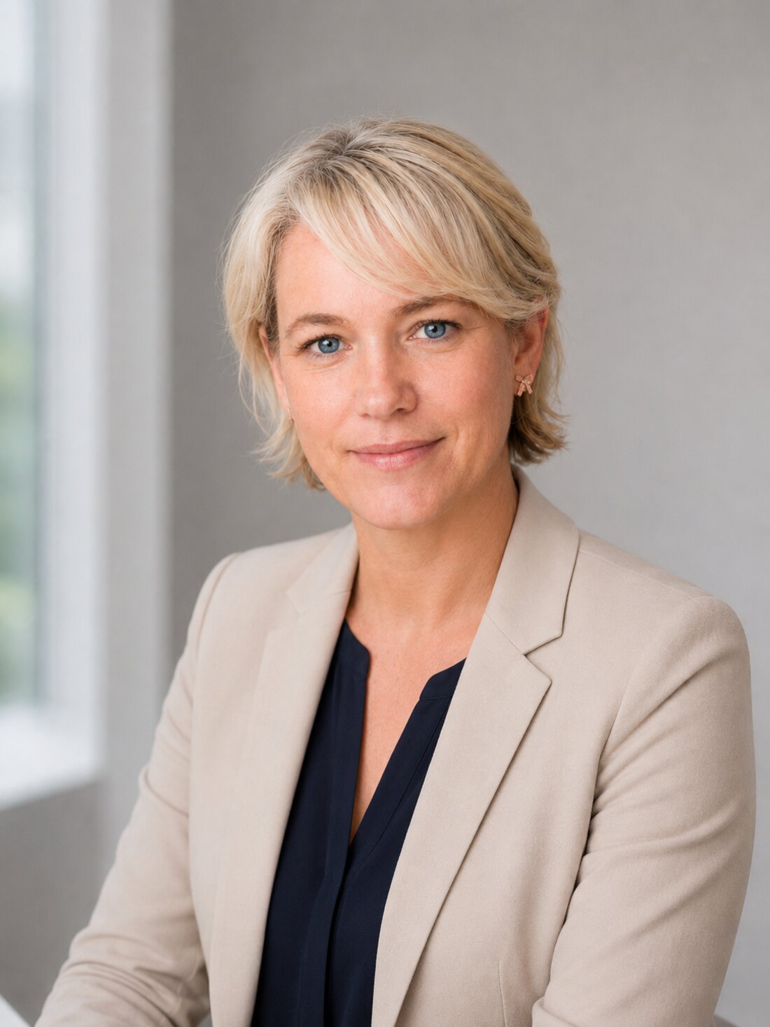 Anna Maria Kaufmann im taupefarbenen Blazer, nachdenklich am Fenster stehend