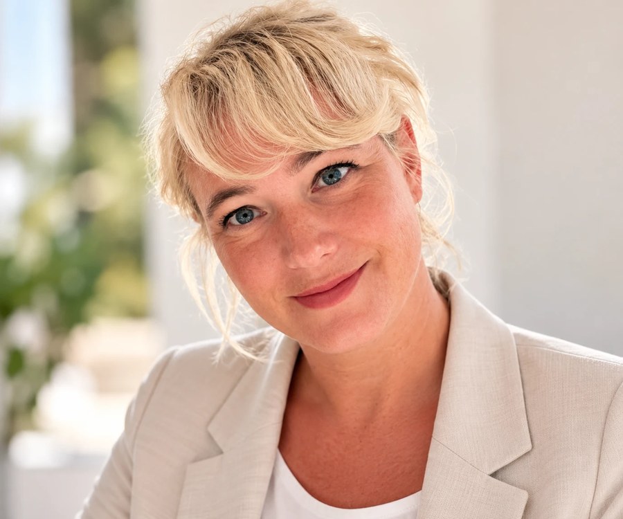 Porträt von Anna Maria Kaufmann in hellem Blazer, lächelnd, den Kopf leicht geneigt, vor hellem sommerlichem Hintergrund